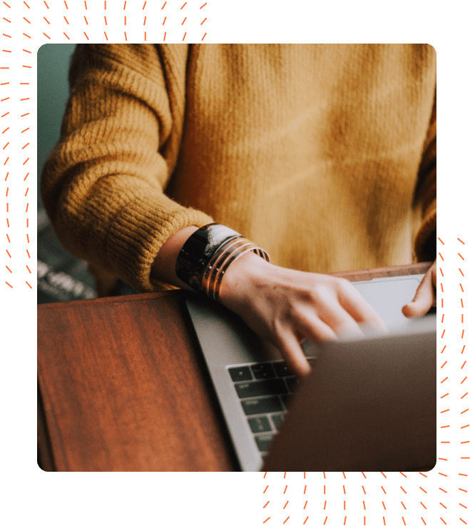 Close-up of a person in a mustard yellow sweater and wearing silver bracelets, typing on a laptop