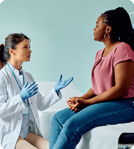 Female doctor sitting on a chair in consultation with a female patient sitting on a hospital bed