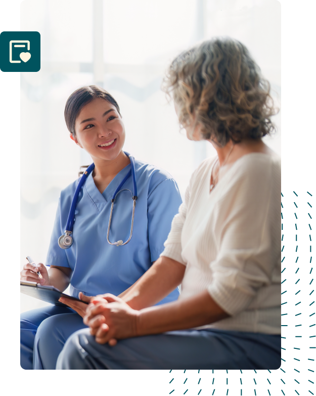 A female doctor wearing blue scrubs smiling warmly at a female patient seated next to them