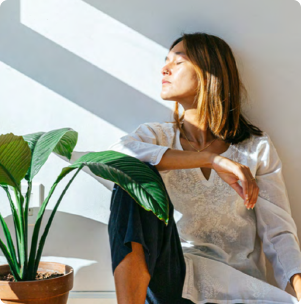 Woman sitting on the floor, leaning against a wall with her face turned to the left and light and shadow falling across her